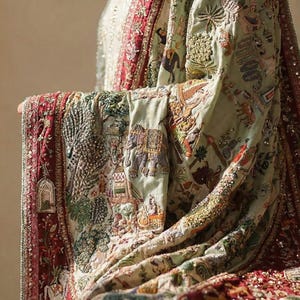 May include: An intricately embroidered textile in shades of green, red, and cream. The fabric features detailed scenes with elephants, figures, and architectural elements. The edges are trimmed with a red border and embellished with beads.