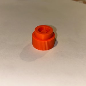 May include: An orange plastic bottle cap with a threaded top and a small hole in the centre.