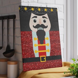 May include: A rectangular cutting board featuring a festive nutcracker design. The nutcracker has a black hat with gold stars, a large mustache, and a red uniform with gold accents. The background is a sparkling red.