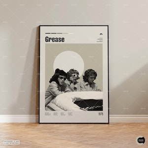 Può includere: Un poster incorniciato con il titolo del film "Grease" e un'immagine in seppia di tre donne con occhiali da sole. Il poster include l'anno 1978 e un elenco di nomi. Lo sfondo è beige chiaro.
