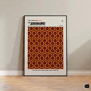 May include: A framed poster featuring the title "The Shining" with the names of the actors. The poster has a repeating geometric pattern in orange, black, and red. The quote "All work and no play makes Jack a dull boy" is at the bottom.