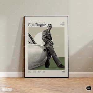 May include: A framed poster featuring the movie "Goldfinger" with a man in a suit leaning against a car. The poster has a minimalist design with text and a color palette of beige, green, and black. The year 1964 is displayed.