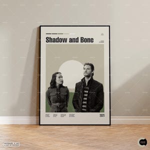 May include: A framed poster featuring the text "Shadow and Bone" above two people. The poster has a neutral color palette with a large white circle and a green stripe. The year "2021" is at the bottom.