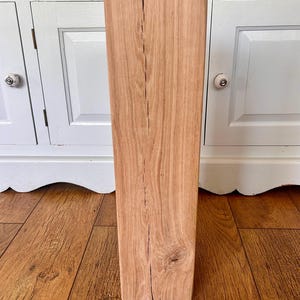 May include: A light-coloured wooden block, rectangular in shape, with a prominent vertical crack and visible wood grain. The block is standing upright, displaying its natural texture and colour.