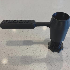 May include: Black 3D-printed tool with the word "FUSION" on the handle. The tool has a cylindrical cup, a handle, and a threaded base with a star-shaped grip. The tool is designed for a specific purpose.