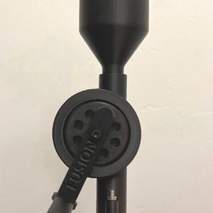 May include: A black reloading tool with a funnel, a wheel with the word "FUSION" on it, and a handle. The base is orange. This tool is used for reloading ammunition.