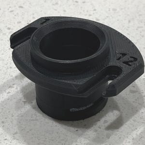 May include: A black, 3D-printed object with a cylindrical base and a wider, curved top. The top has two small cutouts and the number "12" printed on it. The object appears to be a connector or adapter.