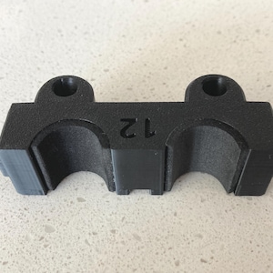 May include: A black, rectangular object with two rounded cutouts and two circular holes on top. The number "12" is embossed on the front. The object appears to be made of a matte, textured material.