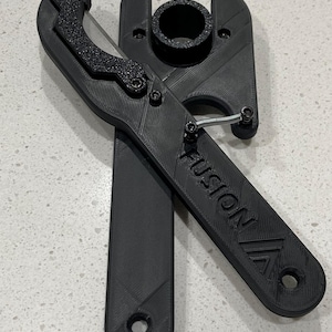 May include: Black plastic tool with a curved blade and a circular opening. The tool has the word "FUSION" embossed on one arm. The blade has a textured grip. The tool is designed with a hinge and spring mechanism.