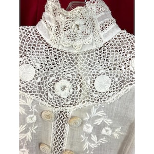 May include: White crochet lace trim with a high neckline and floral embroidery. The lace is delicate and intricate, with a variety of patterns and textures.