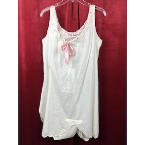 May include: A white vintage slip dress with a scoop neckline and a pink ribbon bow. The dress has a scalloped trim along the neckline and straps. The fabric appears to be lightweight and slightly textured.