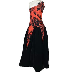 May include: A one-shoulder formal gown featuring a vibrant orange bodice adorned with a black floral pattern. The skirt is a flowing black velvet, creating a striking contrast. The dress has a unique asymmetrical design, perfect for special occasions.