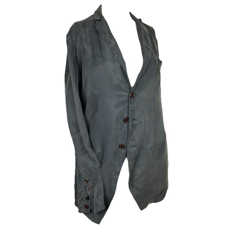 May include: A dark gray blazer featuring a notched lapel, a three-button front closure, and long sleeves with four small buttons on each cuff. The garment has a smooth, slightly textured appearance with a structured collar and a straight hemline.