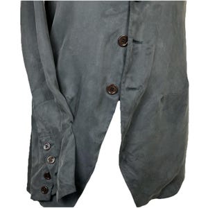 May include: A dark gray blazer featuring a front button closure and long sleeves with four matching dark brown buttons on each cuff. The garment has a smooth, matte texture and a structured design with a visible placket and buttonholes.