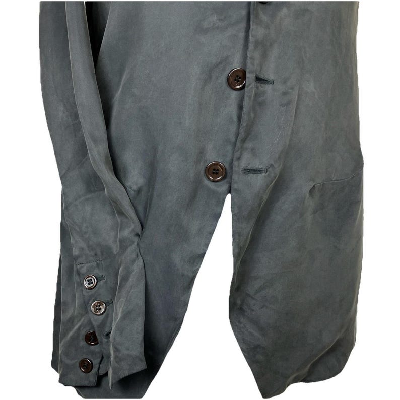May include: A dark gray blazer featuring a front button closure and long sleeves with four matching dark brown buttons on each cuff. The garment has a smooth, matte texture and a structured design with a visible placket and buttonholes.