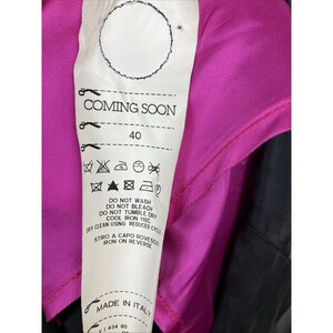 May include: A white fabric garment care label attached to a bright magenta and black textile. The label features the text COMING SOON, the number 40, and various laundry instruction symbols. It also includes the text MADE IN ITALY and iron instructions.