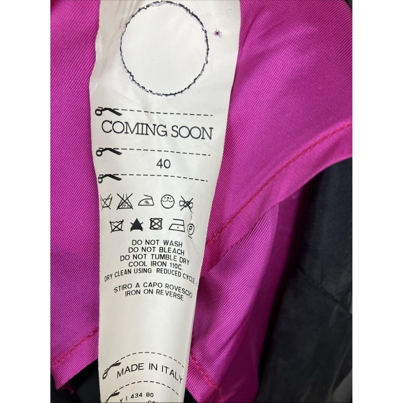 May include: A white fabric garment care label attached to a bright magenta and black textile. The label features the text COMING SOON, the number 40, and various laundry instruction symbols. It also includes the text MADE IN ITALY and iron instructions.