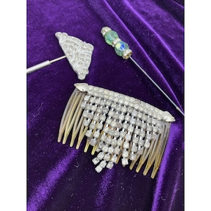 May include: An assortment of vintage hair accessories, including a rhinestone-studded hair comb, a decorative hat pin, and a beaded stick pin. The items are displayed on a purple velvet surface.