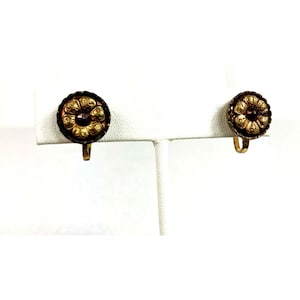 May include: A pair of gold tone clip-on earrings with a dark brown center and a raised floral design.