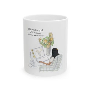 May include: White ceramic mug featuring an illustration of a person working at a desk with a computer and sunflowers. The mug has the text "This week's goal: Do the things that make you happy."