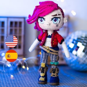 May include: A handmade crochet doll with pink hair, blue eyes, and a red jacket. The doll is wearing a white and blue striped shirt, gray pants, and blue boots. The doll has a nose ring and a tattoo under its eye. The doll is standing on a blue surface.