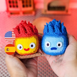 May include: Two handmade crochet figures, one yellow and red, the other blue. The yellow figure has a smiling face and sits on a brown base. The blue figure has a neutral expression. Both have large, round eyes.