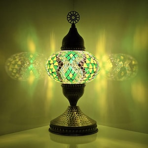 May include: A green and yellow mosaic glass table lamp with a hammered metal base. The lamp is lit and casting a warm glow.