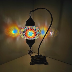 May include: A colorful mosaic glass lamp with a curved metal arm and a black base. The lamp is lit and casting a warm glow.