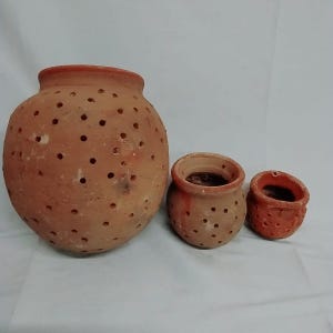 May include: Three terracotta pots of varying sizes. The largest is round with numerous small holes. The other two are smaller, with the smallest having a textured surface. All have a reddish-brown color.