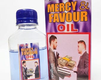 May include: A clear plastic bottle filled with light blue liquid, featuring a blue cap and a label reading DR. JAY MERCY & FAVOUR OIL. Beside it stands a rectangular box with the same text and an image of two people exchanging stacks of cash.
