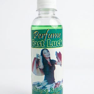 May include: A clear perfume bottle with a white cap, containing green liquid. The label reads "Perfume Fast Luck" and "Chance Rapide Le Parfum" with an image of a woman holding shopping bags. The bottle is on a white background.