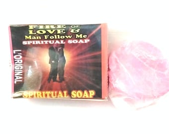 May include: A bar of pink soap next to a box with the text "FIRE OF LOVE & Man Follow Me SPIRITUAL SOAP". The box has a red and black design with an image of two people. The text "L'ORIGINAL" is on the side.