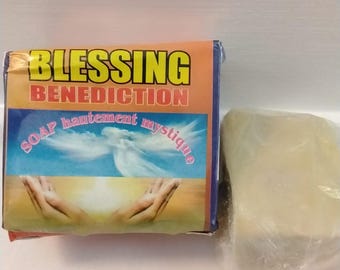 May include: A bar of soap with packaging that reads "BLESSING BENEDICTION" in gold and red lettering. The packaging features an image of hands reaching up towards a dove and the words "SOAP hautement mystique". A second, unwrapped bar of soap is also visible.