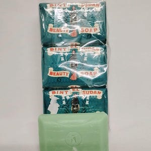 Può includere: Tre saponette verdi e bianche avvolte in plastica con la scritta "Bint El Sudan Beauty Soap" sul davanti. Una singola saponetta verde è visibile nella parte inferiore dell'immagine.