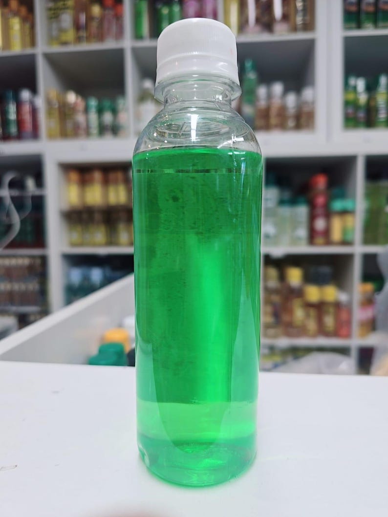 May include: A clear plastic bottle with a white cap, filled with a vibrant green liquid. The bottle is cylindrical and sits on a white surface. The background shows shelves with various bottles.