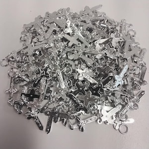 Può includere: Un mucchio di piccoli ciondoli a forma di croce color argento. Le croci hanno vari disegni, alcuni raffiguranti Gesù. Ogni ciondolo ha un piccolo anello per il fissaggio a gioielli o altri lavori artigianali. I ciondoli sono sparsi su una superficie bianca.