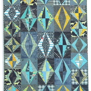 Puede incluir: Una colcha rectangular con un patrón repetitivo de diamantes construido a partir de varios cuadrados de tela. El diseño incorpora una mezcla de textiles azules, amarillos, negros y blancos con diversos estampados que incluyen lunares, rayas y motivos animales.