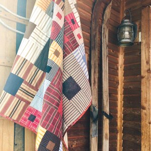 May include: A patchwork quilt featuring a variety of fabric squares in red, yellow, blue, brown, and white. The quilt displays an assortment of patterns including stripes, solid colors, and small geometric prints, all stitched together in a grid.