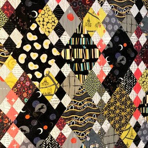 May include: A quilt featuring a diamond-patterned patchwork design. The fabric squares display diverse prints including black and white newspaper text, yellow fried eggs, crescent moons, geometric lines, and abstract patterns in black, yellow, and red.