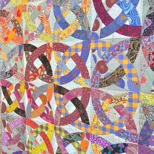 May include: A quilt featuring a repeating Celtic knot pattern constructed from various fabric scraps. The design incorporates a wide array of colors including red, blue, yellow, orange, and purple, with diverse geometric and floral prints.