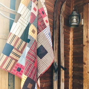 May include: A patchwork quilt featuring a variety of fabric squares in shades of red, blue, yellow, brown, and white. The quilt displays an assortment of patterns including stripes, plaids, and solid colors, stitched together in a grid-like arrangement.