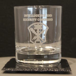 May include: A clear glass tumbler with the words "Intelligence and Security Command" etched on the side. The glass features a white etched emblem with a key, a lightning bolt, and a torch.