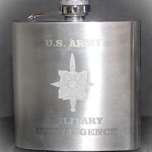 May include: A stainless steel flask with a hinged cap. The flask is engraved with the words "U.S. ARMY" above a military emblem and the words "MILITARY INTELLIGENCE" below. The flask has a brushed metal finish.