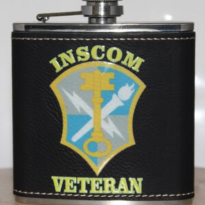 May include: Black leather-wrapped flask with a silver cap. The flask features a colorful emblem with the text "INSCOM VETERAN". The emblem includes a key, lightning bolts, and a torch.