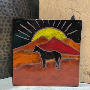 May include: Square ceramic tile featuring a black horse silhouette against a sunset scene. The design includes a yellow sun, red and orange mountains, and a black sky. The tile has a glossy finish and is likely for decorative use.