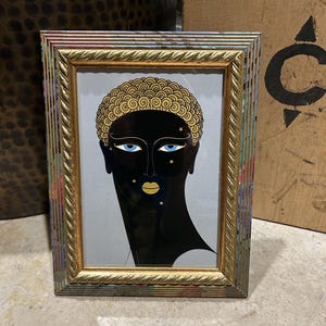 May include: A rectangular picture frame with a gold twisted inner border and a multi-colored outer edge. The frame contains an illustration of a person with black skin, gold curly hair, bright blue eyes, and gold lips, accented by small gold stars.