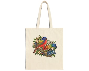 Pode incluir: Uma sacola de lona bege com uma ilustração colorida de um pássaro pousado em um galho com flores. O gráfico inclui o texto Too Colorful To Be Real em uma fonte estilizada e multicolorida, centralizado na parte frontal da sacola.