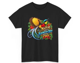 Pode incluir: Uma t-shirt preta com uma ave-do-paraíso colorida de asas amarelas e castanhas, peito vermelho e cauda azul comprida. O gráfico inclui folhagem verde e o texto "NATURE REALLY SHOWED OFF WITH THIS ONE" em letras estilizadas.