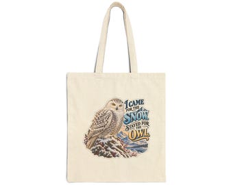 Pode incluir: Uma sacola de lona cor de creme com um gráfico de uma coruja-das-neves pousada em uma rocha. O texto diz I CAME FOR THE SNOW STAYED FOR THE OWL em letras azuis e douradas, contra um fundo de montanhas nevadas e pinheiros.