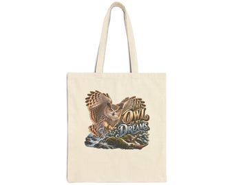 Pode incluir: Uma sacola de lona bege com uma ilustração gráfica de uma coruja marrom em voo sobre um riacho rochoso. O texto THE OWL OF MY DREAMS está impresso em uma fonte estilizada ao lado da coruja. A bolsa tem duas alças longas.